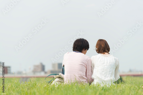 芝生に座り寄り添うカップル © Paylessimages