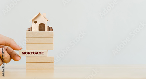Fotografija Hand putting wooden block with word mortgage and wood house with coins stack on top