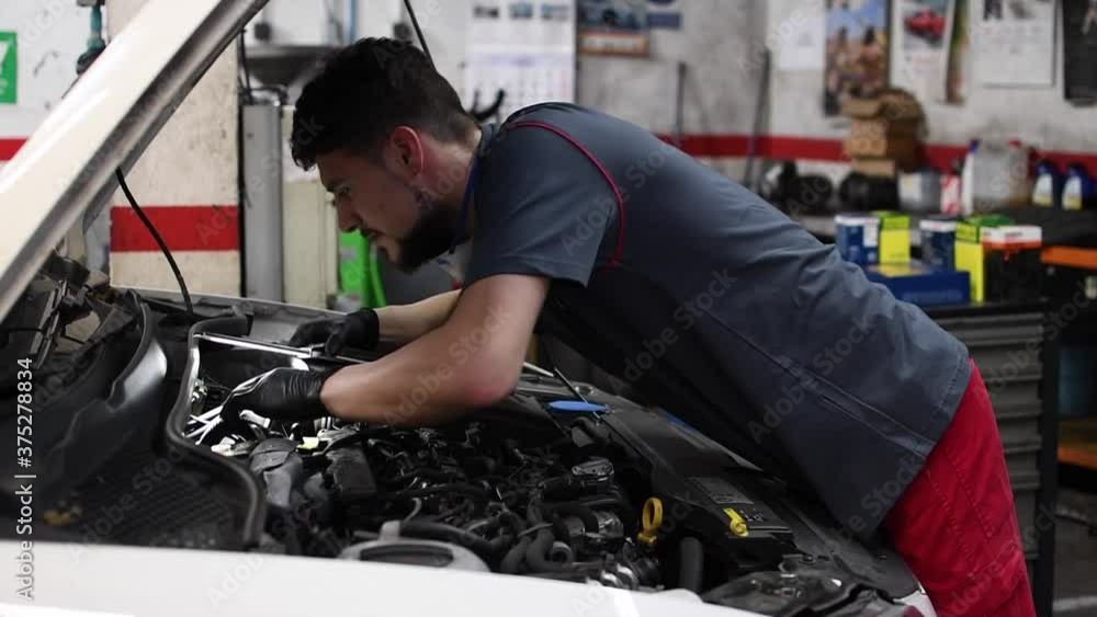Mechanic fixing the engine of a car reclining on it with a flashlight and black latex gloves. truck slider camera movement Mechanic fixing the engine of a car reclining on it with a flashlight and black latex gloves. truck slider camera movement