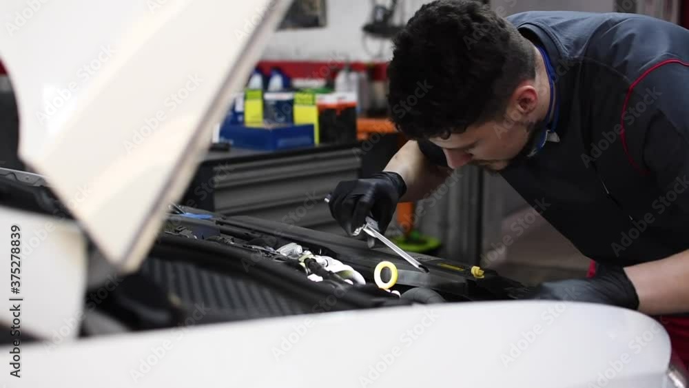 Mechanic inspecting and fixing the engine of a broken down car with a flashlight in hand. Static camera shot. Mechanic inspecting and fixing the engine of a broken down car with a flashlight in hand. Static camera shot.