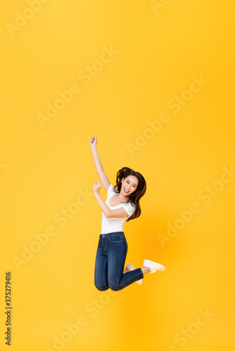 Full length portrait of pretty Asian woman smiling and jumping in mid-air isolated on yellow background