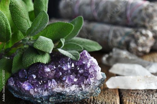 A close up image of an brilliant amethyst geode and white sage on a dark wooden table.  photo