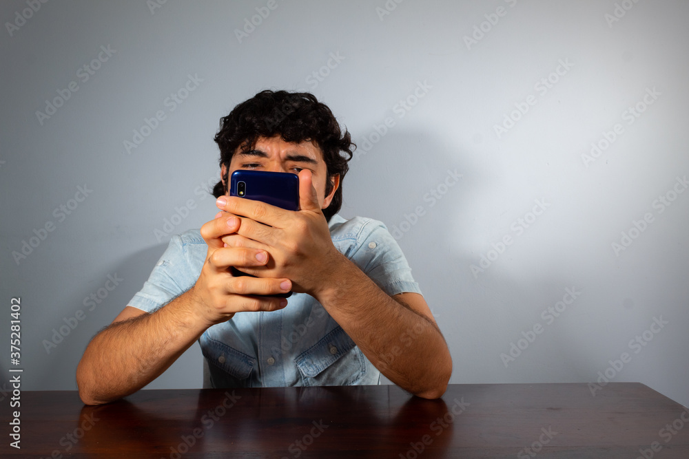Wavy hair young hispanic man using smart phone and showing various emotions Wavy hair young hispanic man using smart phone and showing various emotions