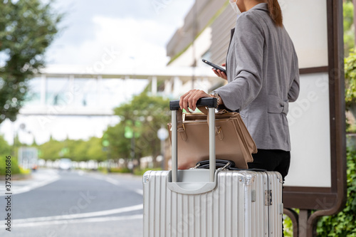 バス停でスーツケースを持ってバスを待つ女性