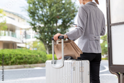 バス停でスーツケースを持ってバスを待つ女性