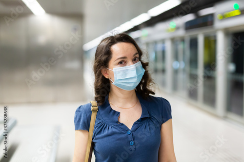 Attractive woman wearing medical mask and rubber gloves waiting for train in platform of underground station. New life reality during COVID 19 pandemic..