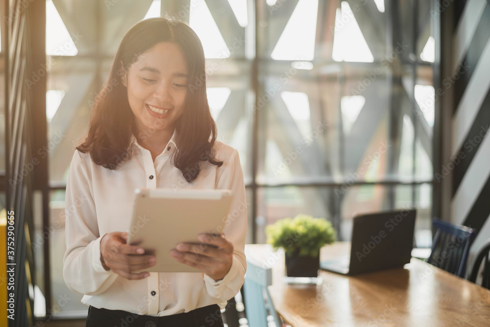 Smiling Asian business woman working on tablet at her desk. Business woman working from home in quarantine. Smiling Asian business woman working on tablet at her desk. Business woman working from home in quarantine.
