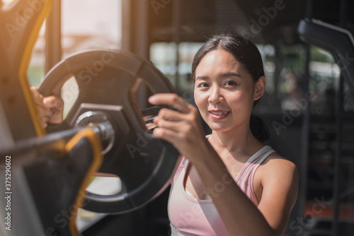 Fit young woman in sportswear working out at the gym. fit asian woman putting more weight splate on barbell photo