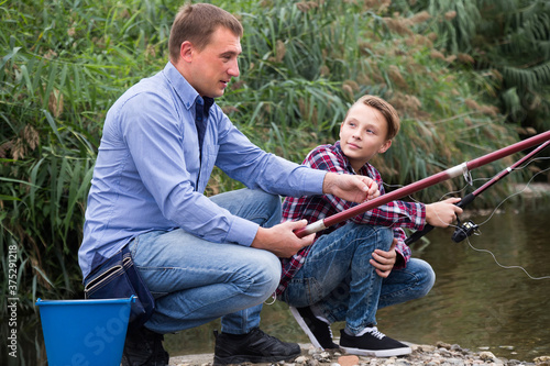 joyful father and teenager son fishing together on lake .