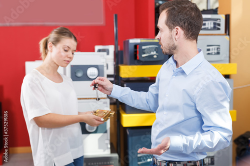 Attractive girl with boyfriend showing keys to their apartment in store on background with safes