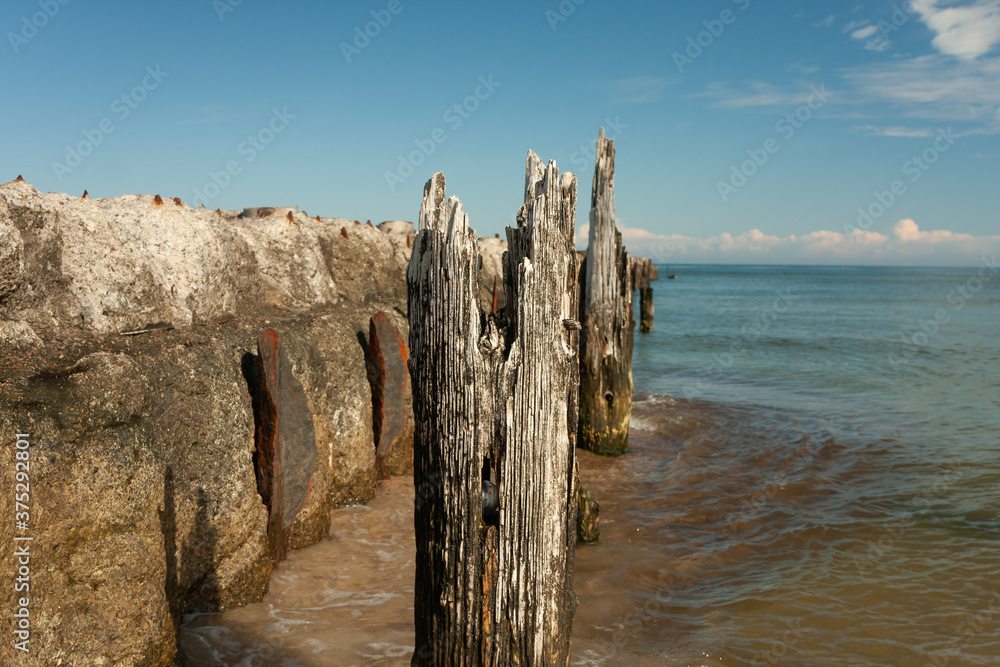 a decaying old concrete breakwater, rusty parts of the structure, old wooden piles stuck in the shore a decaying old concrete breakwater, rusty parts of the structure, old wooden piles stuck in the shore