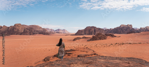 Young Asian traveller with local Arab dress standing on top of mountain and enjoying landscape of Wadi Rum desert, Jordan, Arab. Panoramic banner portion