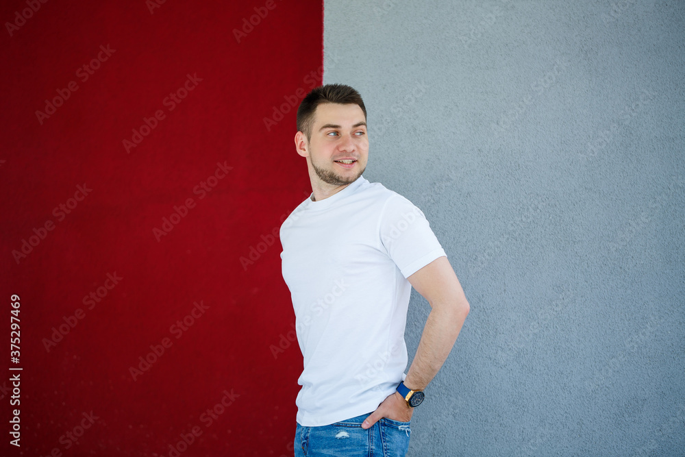 Stylish young man, a man dressed in a white blank t-shirt standing on a gray and red wall background. Urban style of clothes, modern fashionable image. Men's fashion Stylish young man, a man dressed in a white blank t-shirt standing on a gray and red wall background. Urban style of clothes, modern fashionable image. Men's fashion