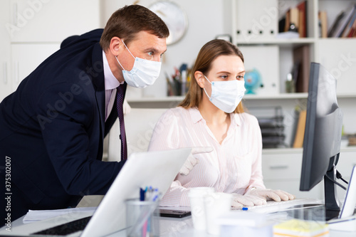 Man in protective medical mask helping his colleague to prepare document on your computer