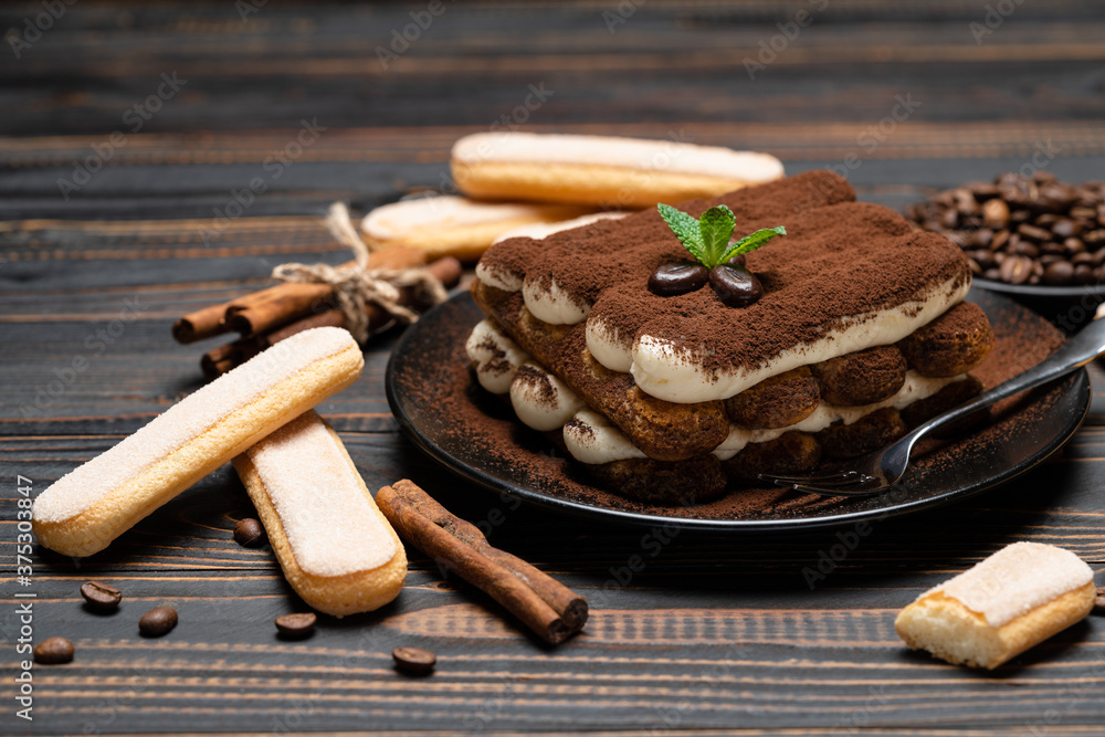 Classic tiramisu dessert on ceramic plate and savoiardi cookies on wooden background Classic tiramisu dessert on ceramic plate and savoiardi cookies on wooden background