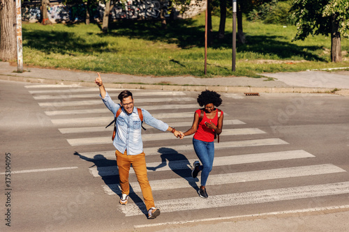 Young cheerful couple running over street and smiling.