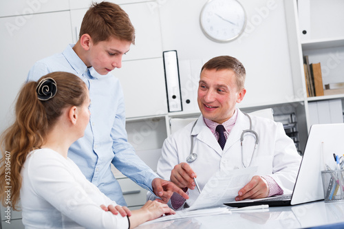 Middle-aged mother and son visiting consultation with man doctor in hospital