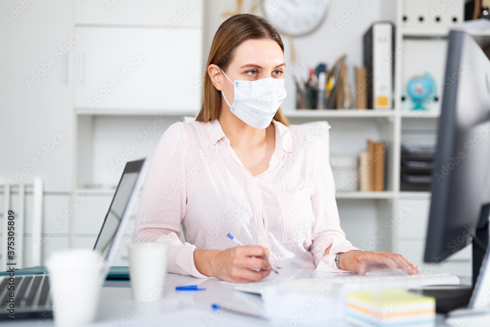 Businesswoman in protective medical mask is working with project behind laptop in the office