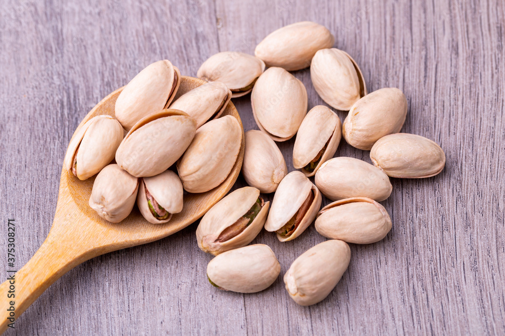 Pistachio in a wooden spoon on grained wood background. Pistachio in a wooden spoon on grained wood background.