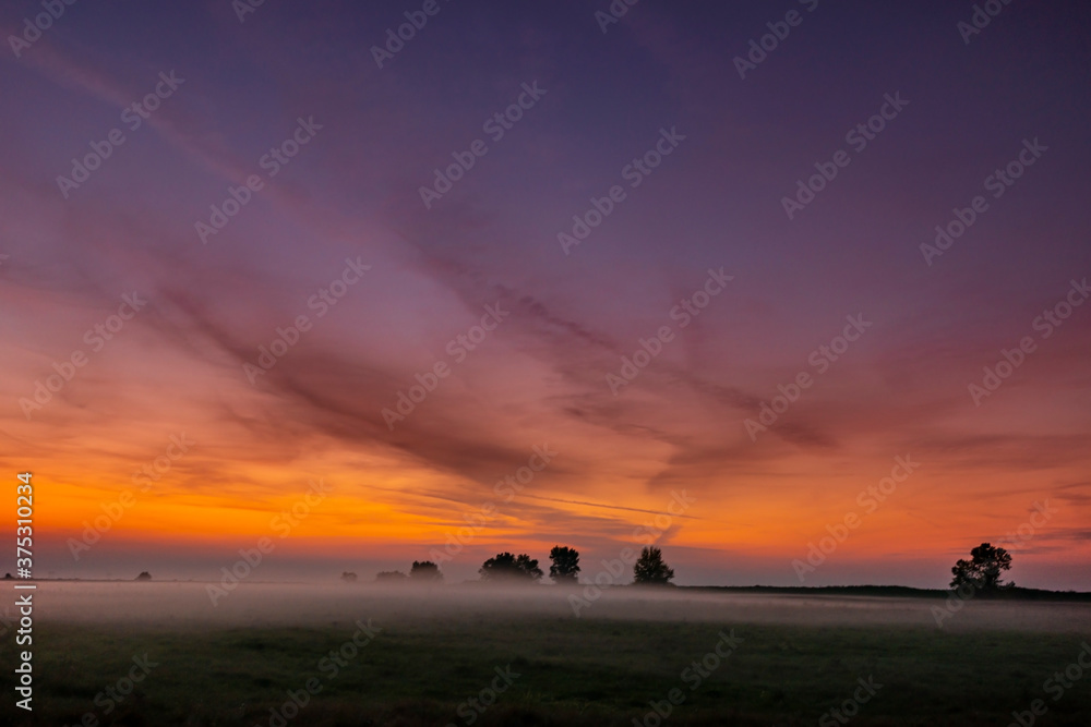 Colorful warm sunset over rural field covered with fog and mist, in autumn