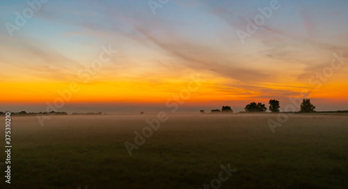 Colorful warm sunset over rural field covered with fog and mist  in autumn
