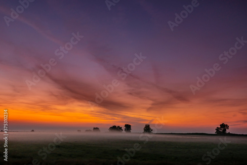 Fototapeta Naklejka Na Ścianę i Meble -  Colorful warm sunset over rural field covered with fog and mist, in autumn