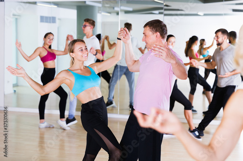 Young smiling men and women dancing swing in dance class. Focus on man