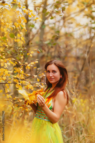 Portrait of pretty young woman of Slavic appearance in yellow colored dress in autumn, walk in forest. Cute model walks in Park in golden autumn against background of nature
