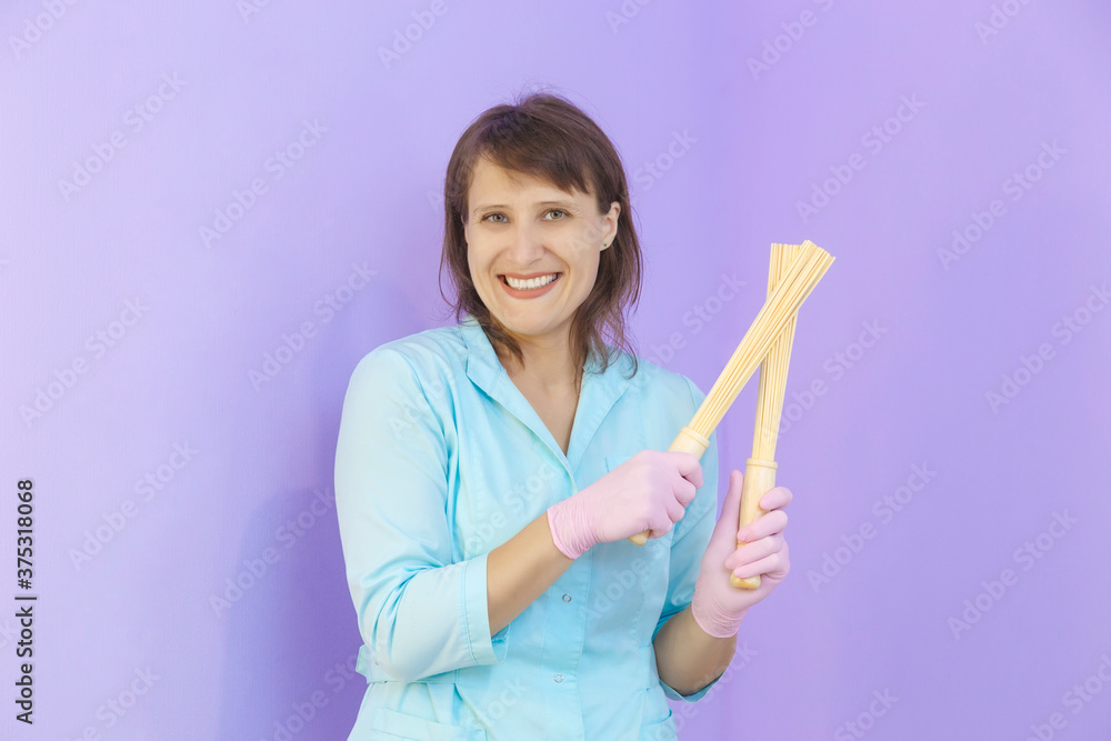 Smiling woman masseuse holding massager sticks in green uniform Smiling woman masseuse holding massager sticks in green uniform