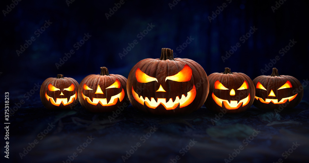 Five spooky halloween pumpkin, Jack O Lantern, with an evil face and eyes on the forest floor at night with a dark background. Five spooky halloween pumpkin, Jack O Lantern, with an evil face and eyes on the forest floor at night with a dark background.