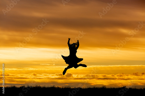 夕陽を背景に元気よくジャンプする女性のシルエット