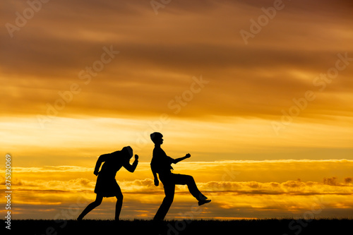 Fototapeta Naklejka Na Ścianę i Meble -  夕陽を背景に元気よく歩く男女高校生のシルエット