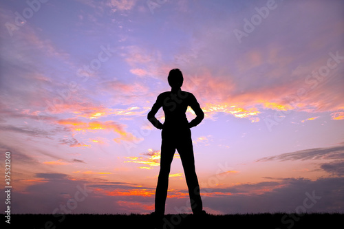 夕陽を背景に腰に手を当て立ち姿の男性のシルエット © chikala