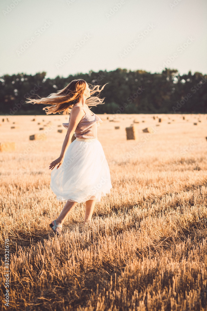 Obraz premium young woman in dress walking in evening in field with hay bales, beautiful romantic girl with long hair outdoors in field