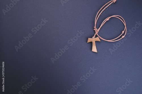Closeup of a wooden tau cross necklace isolated on a dark background