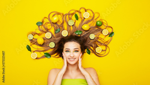 peaceful girl lying on yellow background with citrus fruits in long hair young woman head with lemon slices and leaves