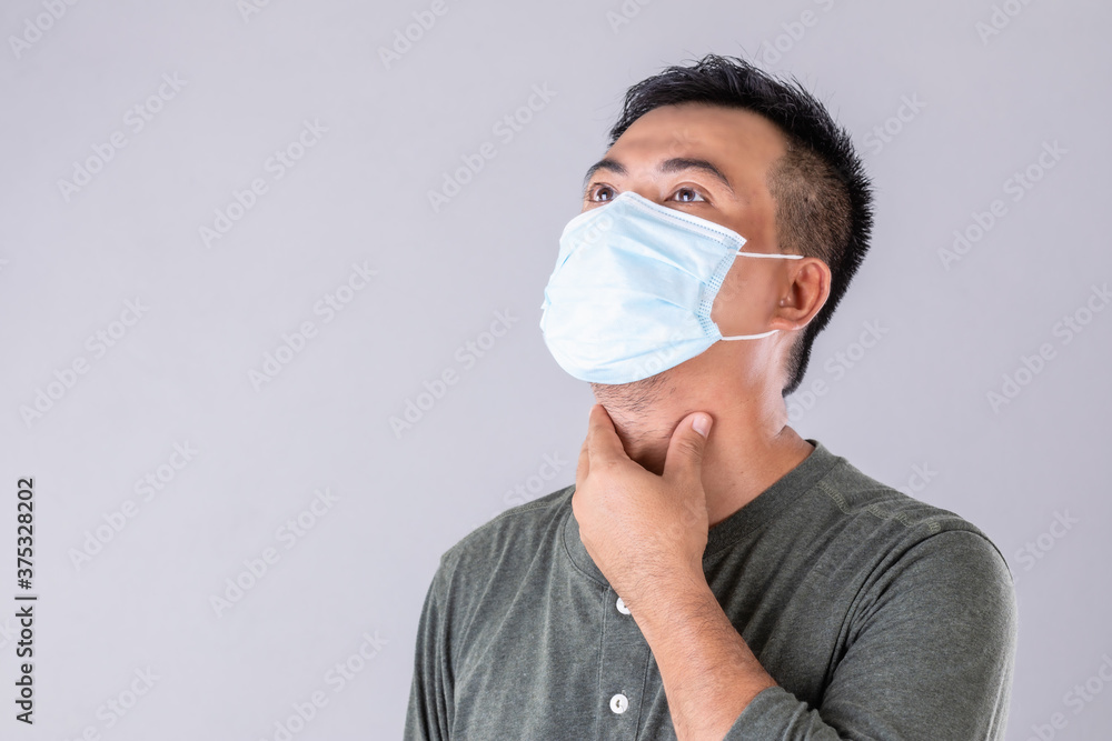 Thai patient wearing protective face mask and touching on his neck studio shot on grey background Thai patient wearing protective face mask and touching on his neck studio shot on grey background