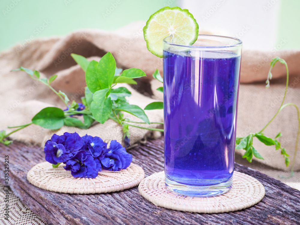Fresh purple Butterfly pea or blue pea flower and juice in glass with lime on wooden table. Fresh purple Butterfly pea or blue pea flower and juice in glass with lime on wooden table.
