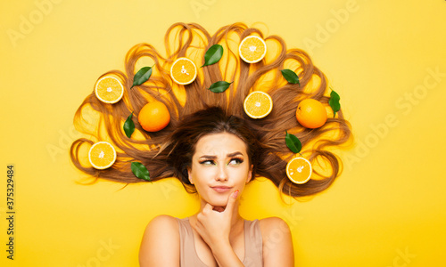 beautiful girl lying on studio background with orange fruits on long hair  young woman head thinking  making choice  view from above
