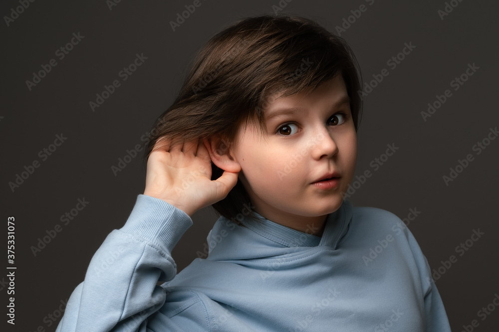 Curious young schoolboy holding hand at his ear, trying to overhear private conversation, dressed in casual clothes Curious young schoolboy holding hand at his ear, trying to overhear private conversation, dressed in casual clothes