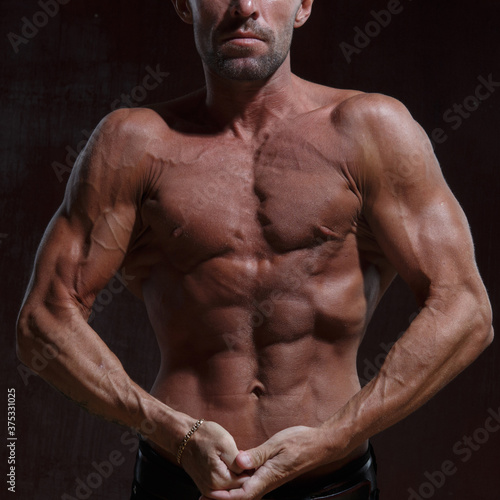 A slender, athletic man with a naked muscular torso on a dark background.