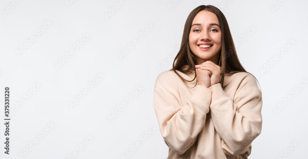 Young happy brunette woman keeps hands together near chin, smiles gently, has cute expression Young happy brunette woman keeps hands together near chin, smiles gently, has cute expression