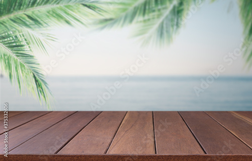 Brown wooden planks with blur beach sky on background and  palm leaves on foreground summer concepts.