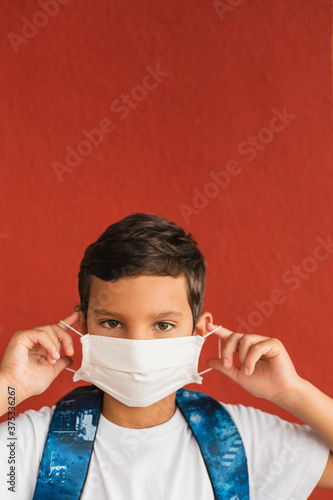 Portrait of caucasian boy of nine years old putting on surgical mask on face looking aside outdoorl. photo