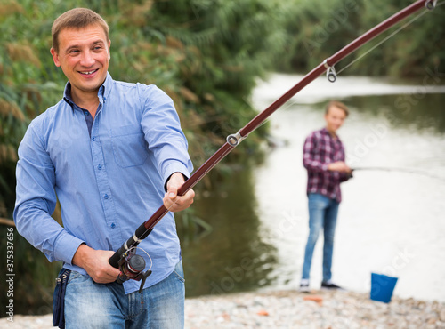 portrait of joyful smiling man casting line for fishing on river .