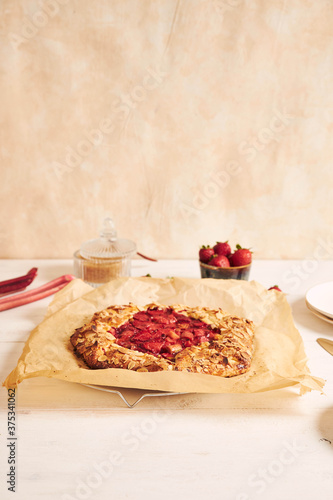 Delicious rhubarb strawberries gallate cake with ingredients on a white table photo