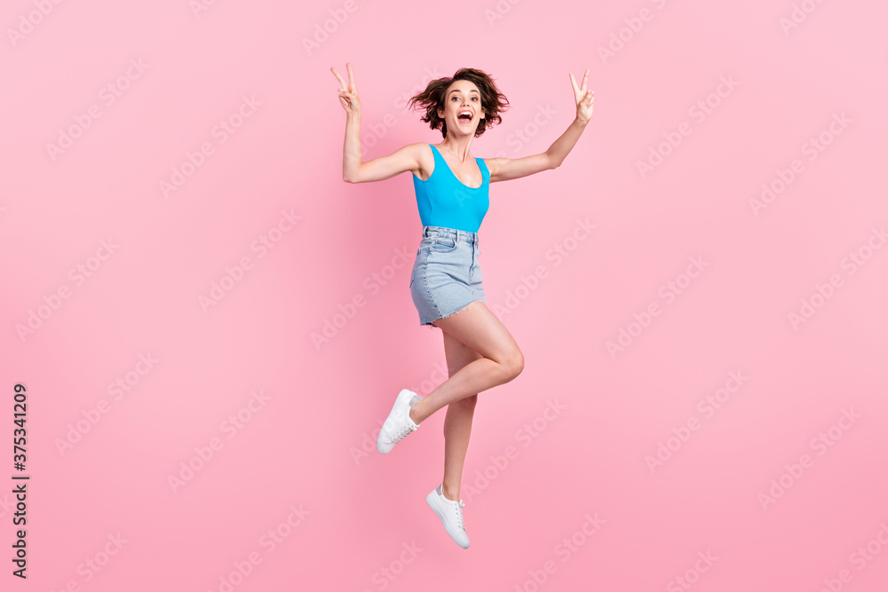 Full body size photo of pretty charming sporty young lady smiling open mouth jump raise hands showing v-sign wear denim mini skirt blue singlet sneakers isolated pink color background