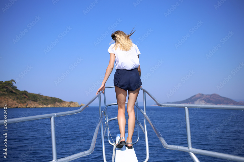 A slender woman stands on the bow of the yacht, her back, traveling across the Mediterranean Sea.