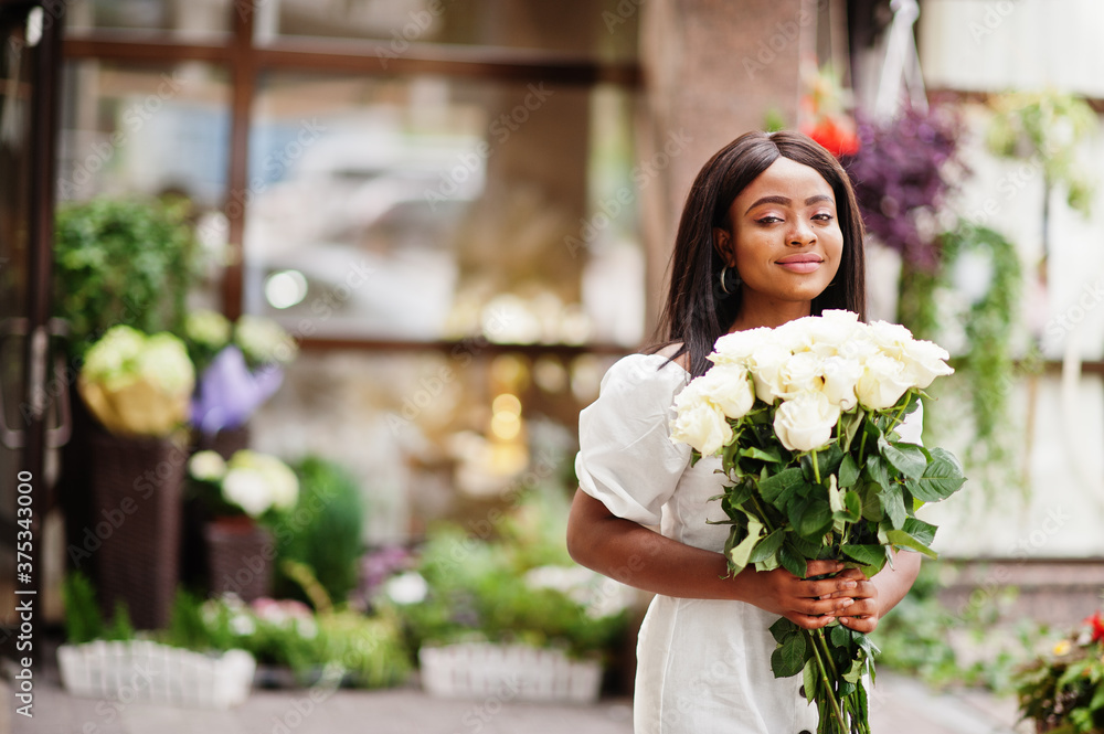 Beautiful african american girl holding bouquet of white roses flowers on dating in the city. Black businesswoman with bunch of flowers.