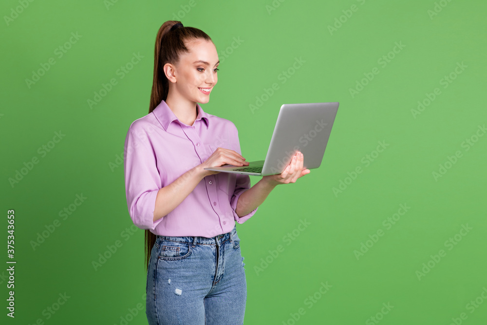 Profile side photo of positive manager girl work remote laptop have wifi connection social networking communication wear lilac violet denim jeans isolated green color background Profile side photo of positive manager girl work remote laptop have wifi connection social networking communication wear lilac violet denim jeans isolated green color background